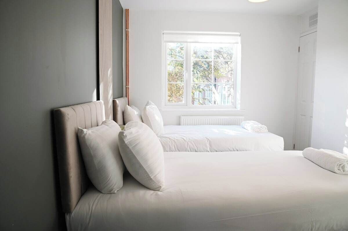 A bedroom with a bed, pillows, a window, and a radiator.