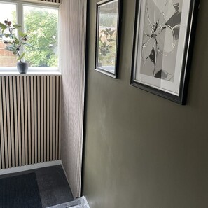 Una habitación con un radiador, una ventana con una planta y dos cuadros en la pared.