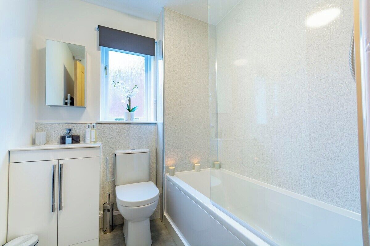 Et moderne badeværelse med toilet, vask, spejl og badekar.