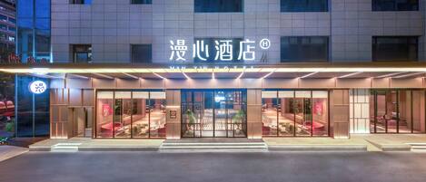 A hotel entrance with a modern facade, large glass doors, and a well-lit interior visible through the doors.