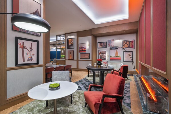 A modern hotel lobby with a round table, red chairs, artwork on the walls, and a fireplace.