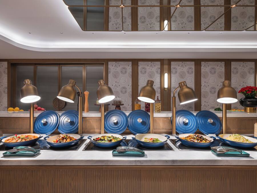 A buffet setup with multiple serving stations, blue serving dishes, and gold-colored lamps.