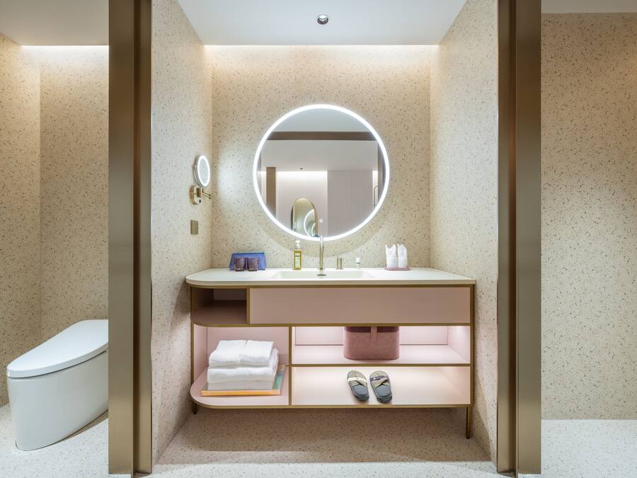 A modern bathroom with a freestanding toilet, a vanity with a mirror, and a built-in shelf for towels and slippers.
