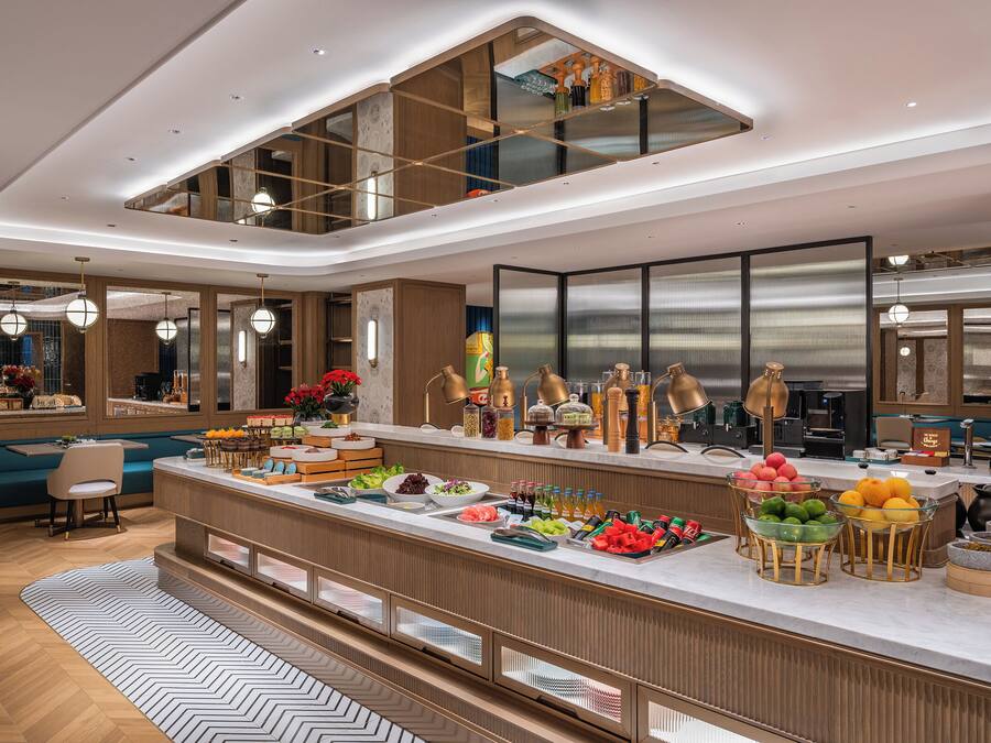 A modern kitchen with a breakfast bar, wooden cabinetry, and a variety of fruits and beverages.