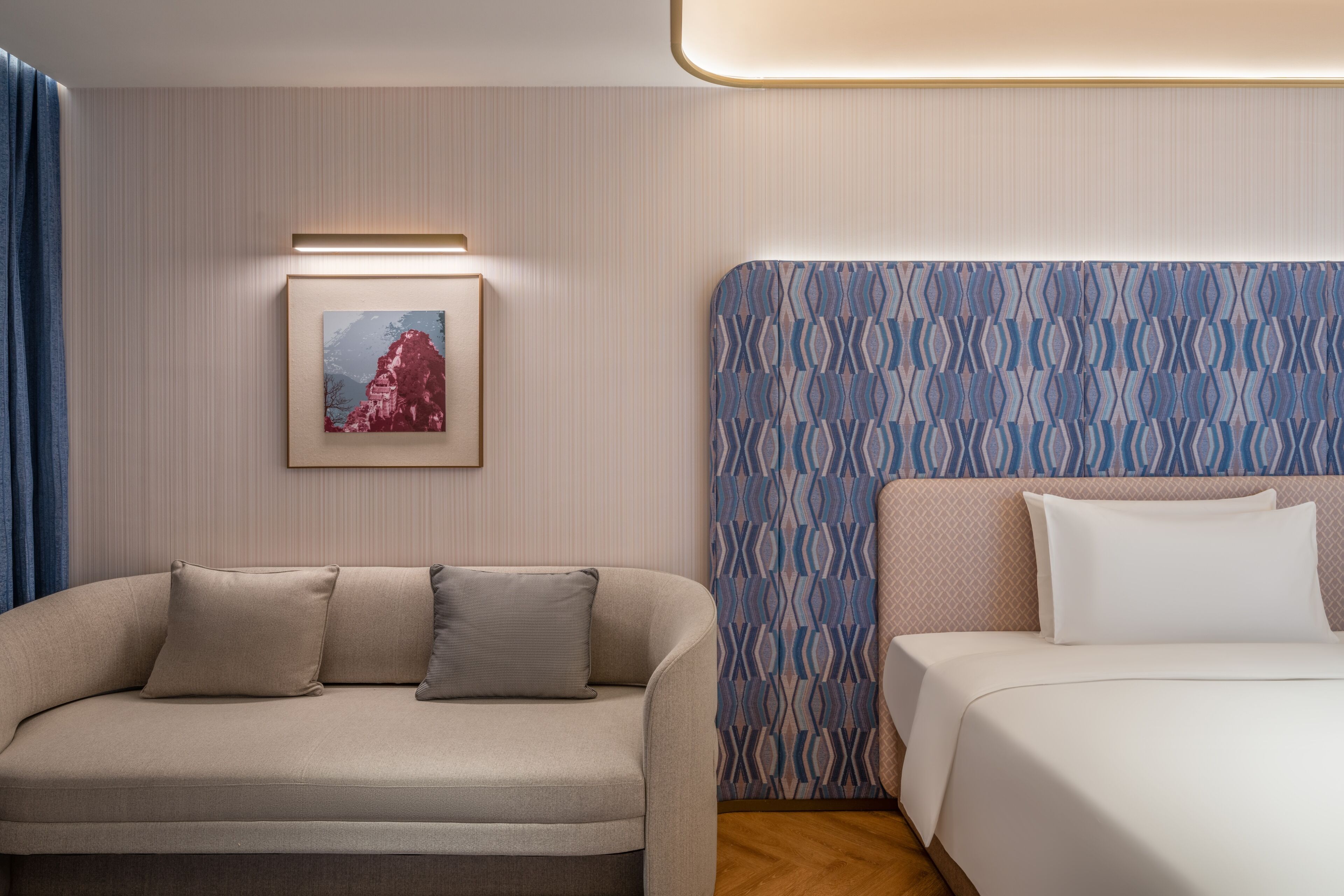 Habitación de hotel con sofá, cama, cabecera estampada y un cuadro en la pared.