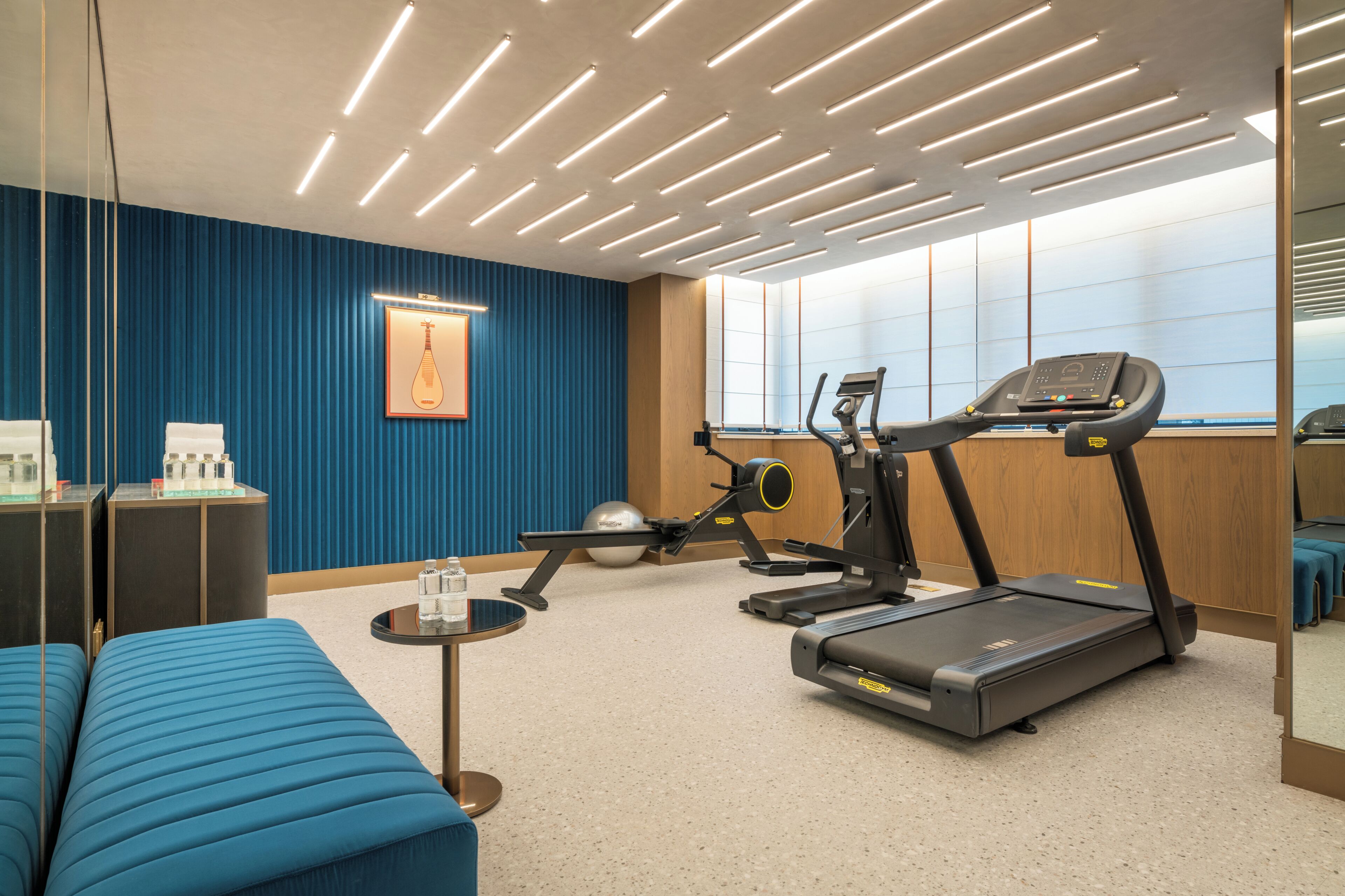 A fitness room with exercise equipment, a blue sofa, and a wall-mounted picture.