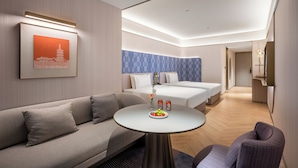 A modern hotel room with a sofa, a round table with fruit, a bed, and a blue patterned wall. - Xi'an Bell Tower Manxin Hotel (Xi'an)