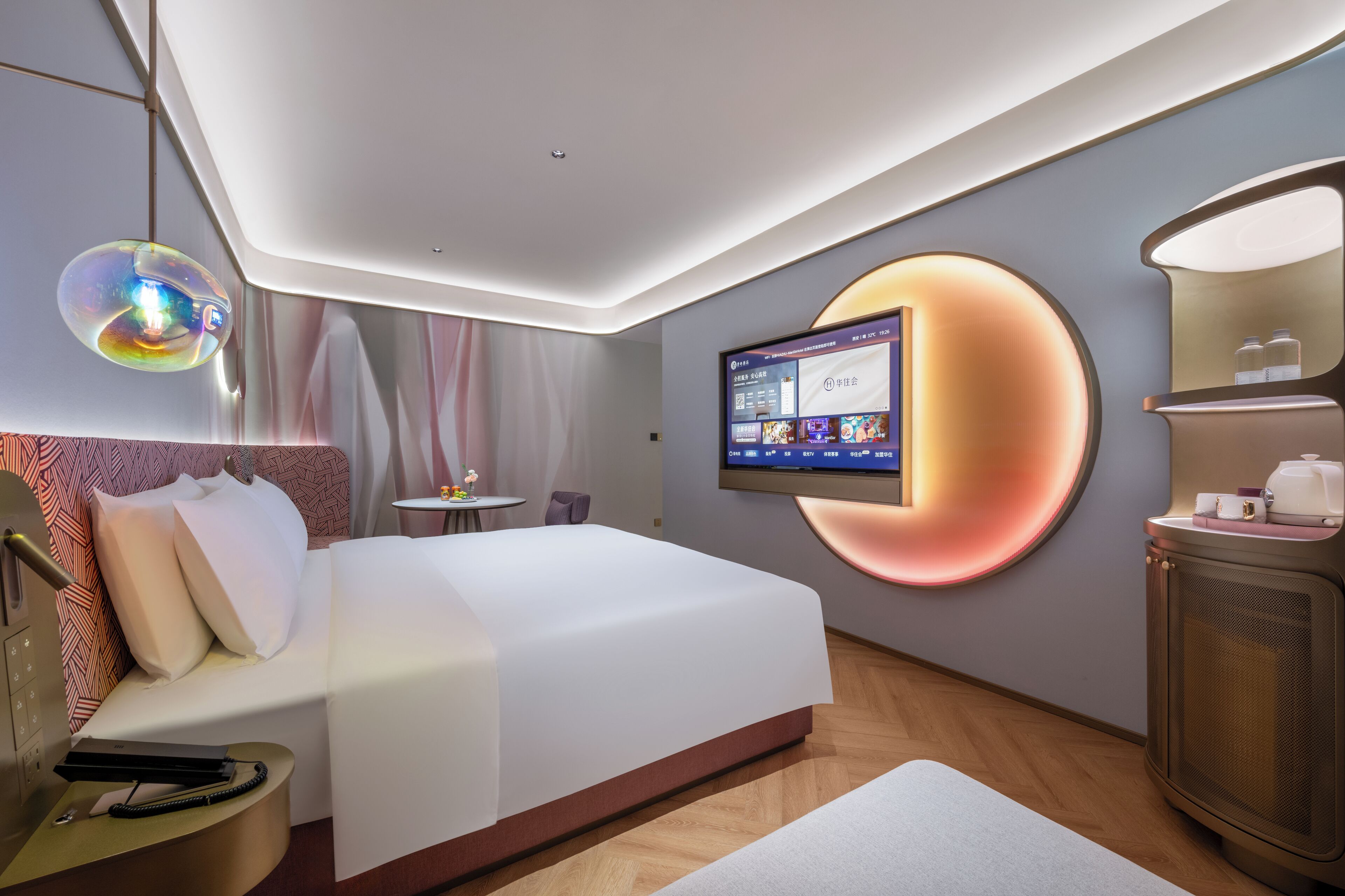 A modern hotel room with a large bed, a desk, a television mounted on the wall, and a minibar.