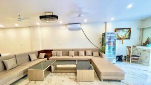 A modern living room with a sectional sofa, a glass coffee table, and a marble floor.