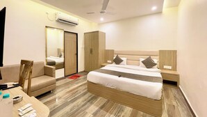 A hotel room with a bed, a desk, a chair, a wardrobe, and an air conditioning unit.