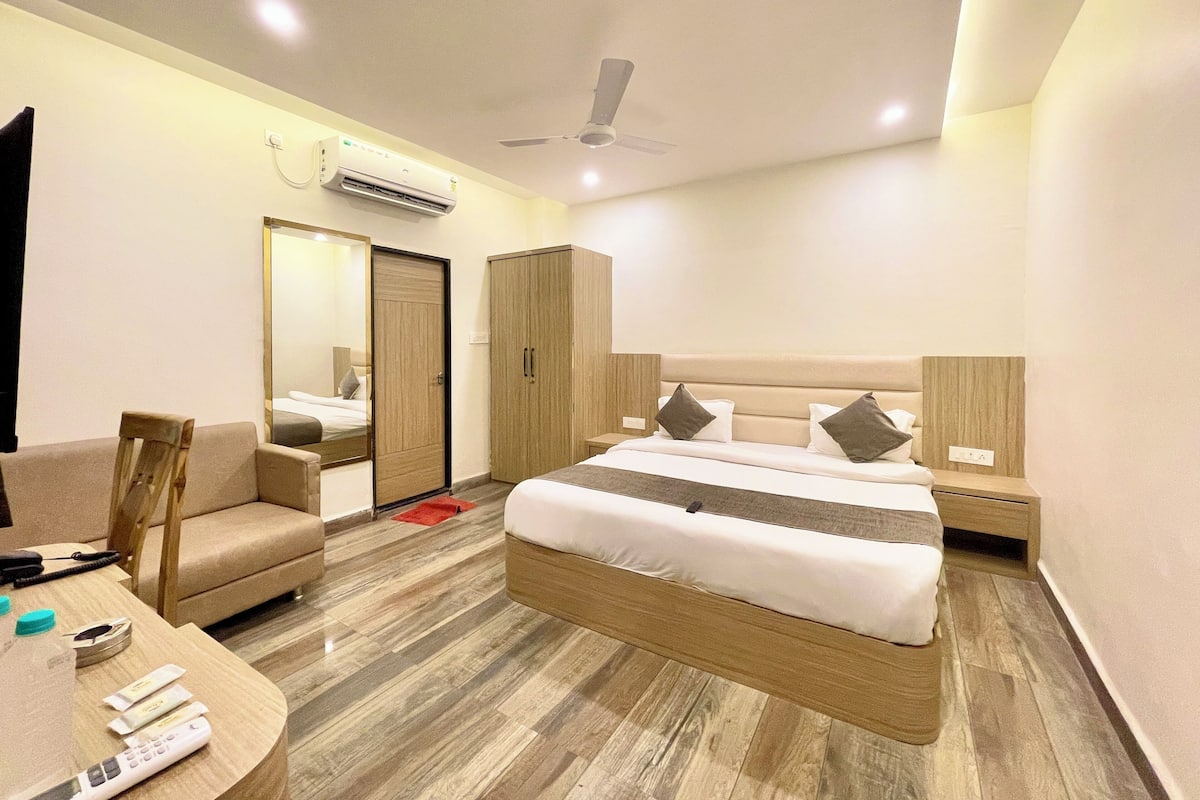 A hotel room with a bed, a desk, a chair, a wardrobe, and an air conditioning unit.
