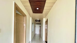 A hallway with wooden doors and a tiled floor, leading to a room with a wooden ceiling and a window.