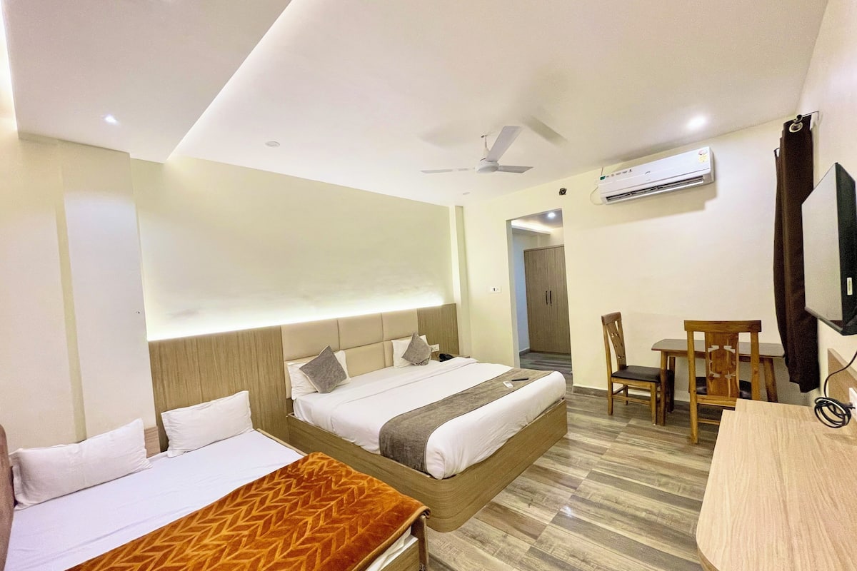 A hotel room with two beds, a desk, a chair, a TV, and an air conditioning unit.