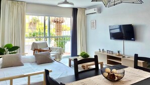 Habitación de hotel con cama, mesa de comedor con sillas, televisor y ventana con cortinas.