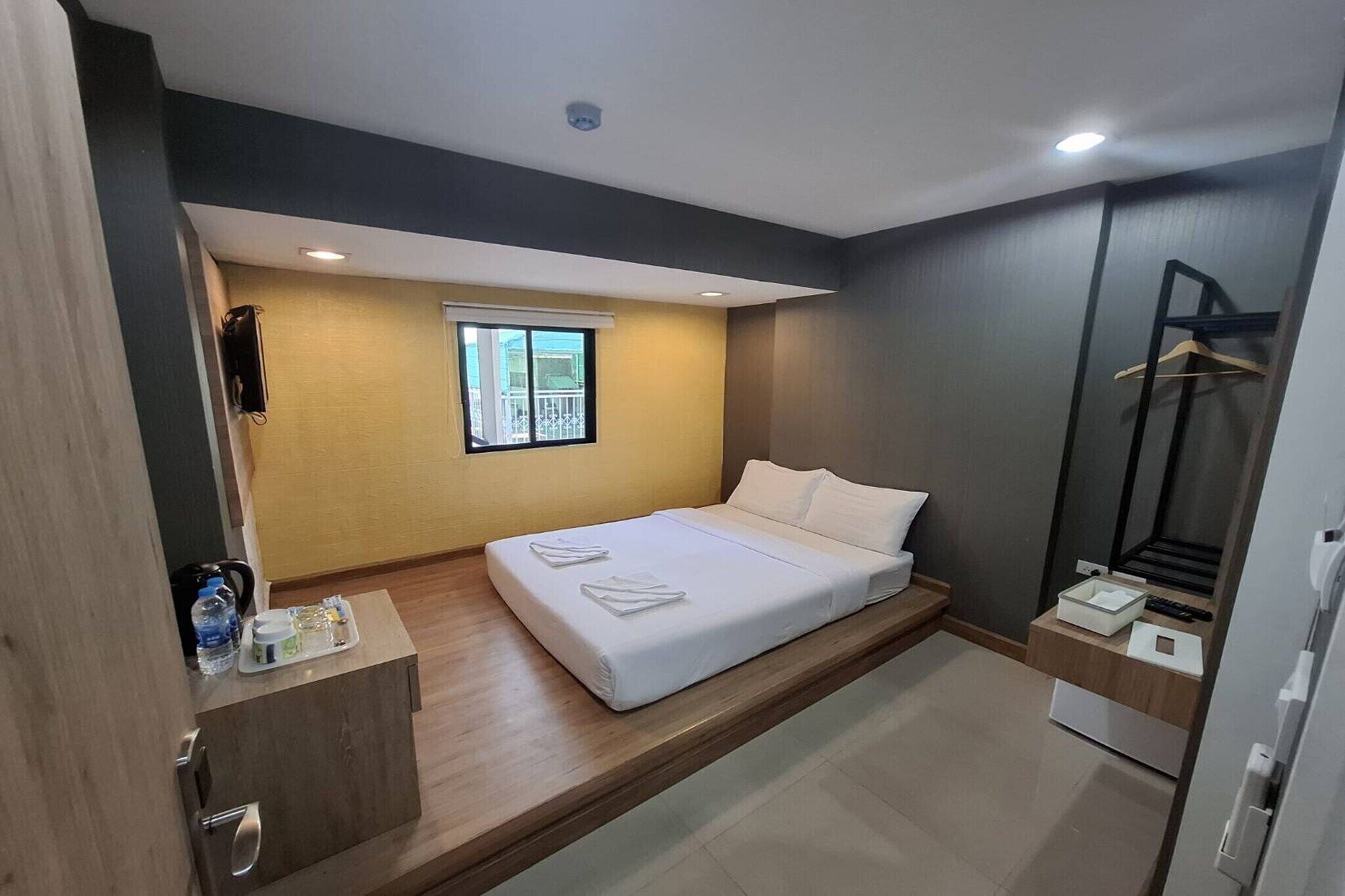 A modern hotel room with a bed, a small desk, a window, and a wardrobe.