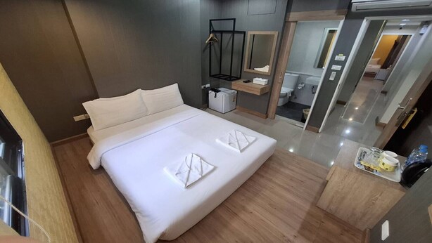 A modern hotel room with a large bed, a bedside table, a mirror, and a small bathroom area.