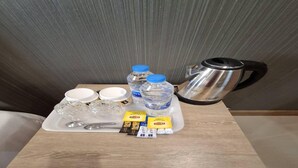 A tray with a kettle, water bottles, cups, a spoon, and packets of snacks on a wooden table.