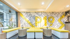 A modern reception area with a geometric wall mural, a central yellow bench, and a glass display case.