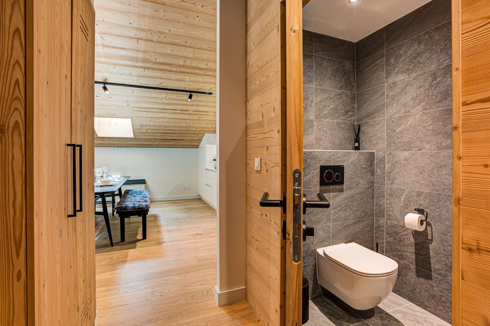 A modern bathroom with a toilet, shower, and wooden door.