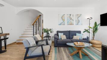 Una sala de estar moderna con una escalera, un sofá gris, una mesa de centro redonda y una planta grande.