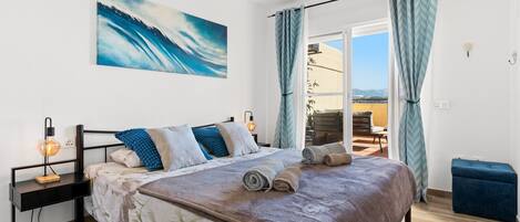A bedroom with a bed, a desk, a chair, a window with curtains, and a painting on the wall.