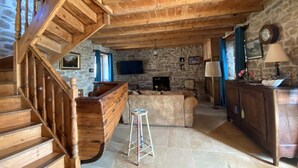 Un escalier en bois rustique mène à un espace de vie doté de murs en pierre, d’une cheminée et d’un téléviseur.