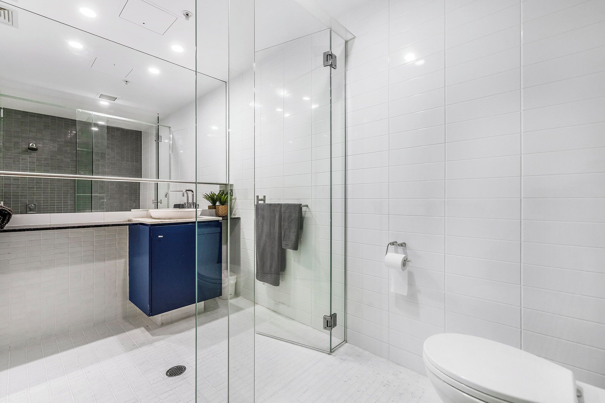 A modern bathroom with a glass shower enclosure, a white toilet, and a blue cabinet.