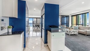 Une cuisine moderne avec des meubles blancs et des touches de bleu, qui donne sur un espace repas offrant une vue sur le paysage urbain.