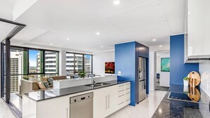 Une cuisine moderne dotée d’un îlot central, d’appareils électroménagers en acier inoxydable et offrant une vue sur le paysage urbain grâce à de grandes fenêtres.