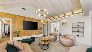 Een moderne woonkamer met een grote flatscreen-tv, comfortabele zitplaatsen, een houten accentmuur en een plafond met zichtbare balken.
