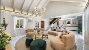 Een ruime woonkamer met een hoge plafond, een trap en een keuken op de achtergrond.