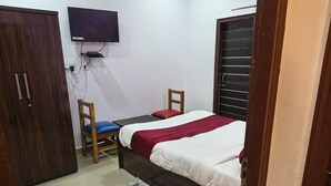 A bedroom with a bed, a chair, a wardrobe, and a television mounted on the wall. - HOTEL TRIMURTI INN (Lucknow)