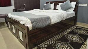 A bedroom with a wooden bed, a dark wooden wardrobe, and a patterned rug. - HOTEL TRIMURTI INN (Lucknow)