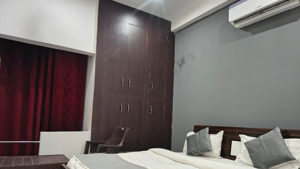 A bedroom with a bed, a chair, a wardrobe, and an air conditioner. - HOTEL TRIMURTI INN (Lucknow)