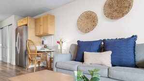 Een moderne woonkamer met een grijze bank, houten kasten, een eethoek en een keuken met een roestvrijstalen koelkast.