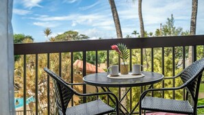 Een balkon met twee rieten stoelen en een klein rond tafeltje, met een vaas met een bloem en twee kopjes.
