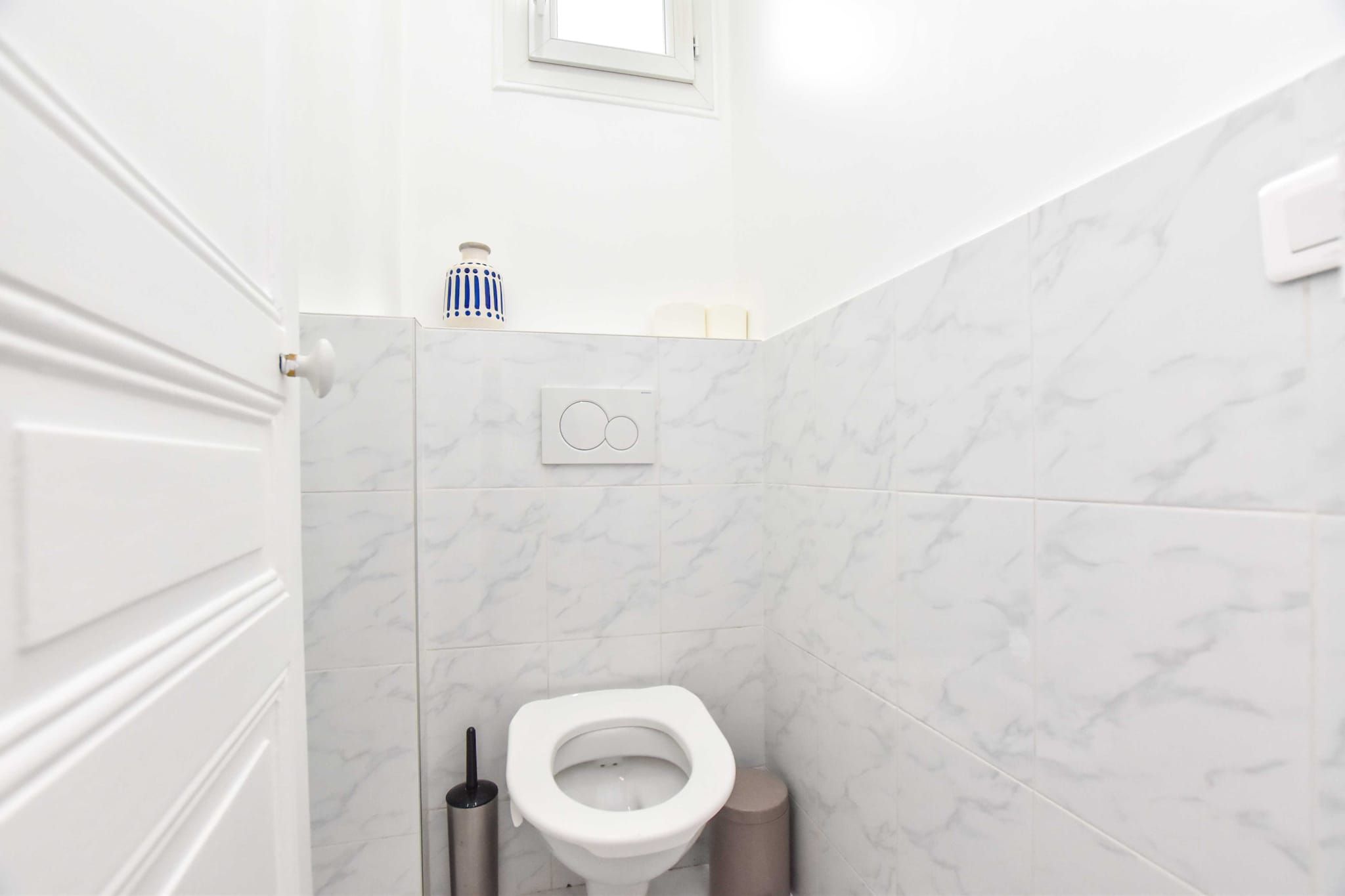 A bathroom with a toilet, a hand dryer, and a trash bin.