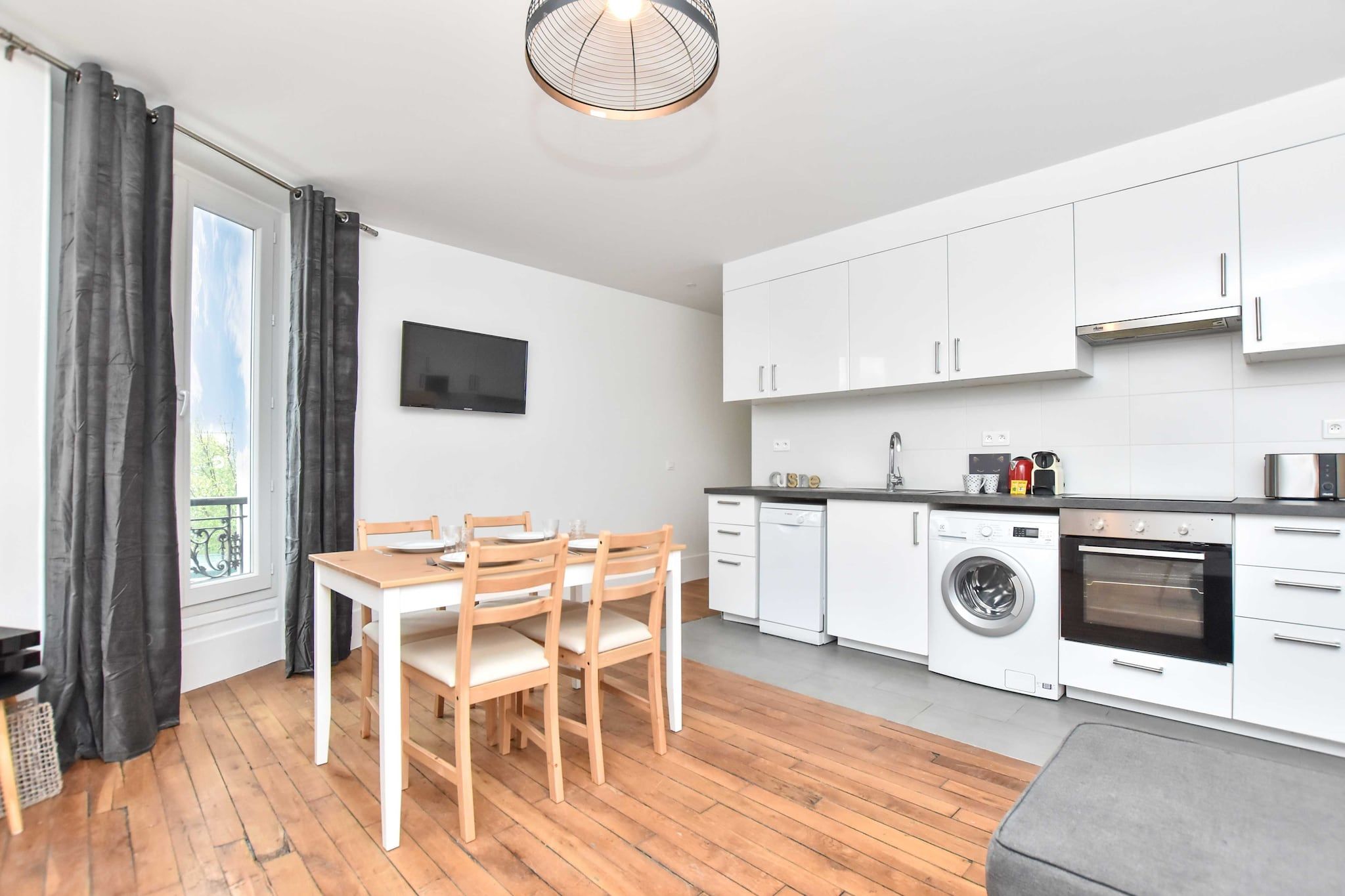 A compact kitchen with white cabinets, a washing machine, an oven, and a dining area with a table and chairs.