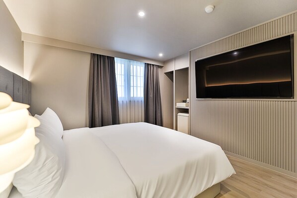 Una habitación de hotel moderna con una cama grande, un televisor de pantalla plana montado en la pared y un escritorio integrado con una silla.