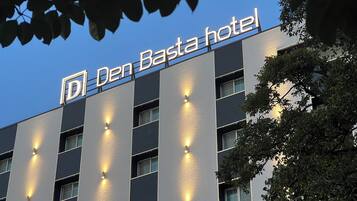 Un edificio de hotel con un cartel que dice "Den Basta hotel" y varias ventanas iluminadas.
