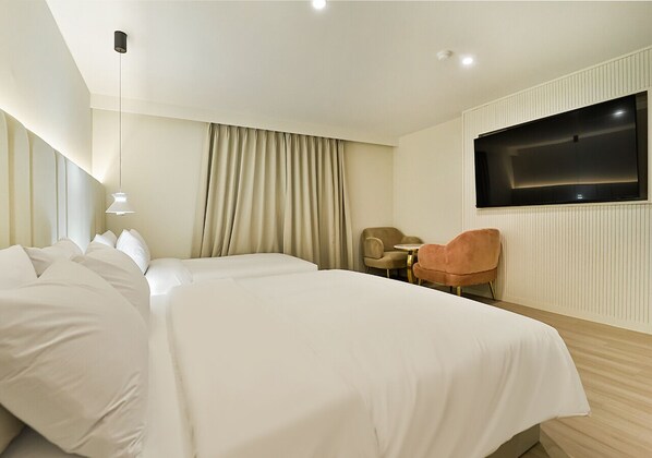 A hotel room with two beds, a TV mounted on the wall, a chair, and a small table.