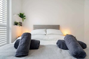 A bed with white linens, grey headboard, and two bedside lamps.