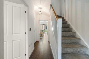A hallway with a staircase, white walls, and a wooden floor.