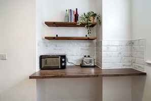 A kitchen with a microwave, toaster, wooden shelves, and a potted plant.