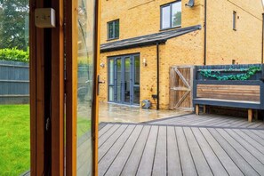 A wooden deck leading to a brick building with a sliding glass door, a wooden fence, and a small garden area.