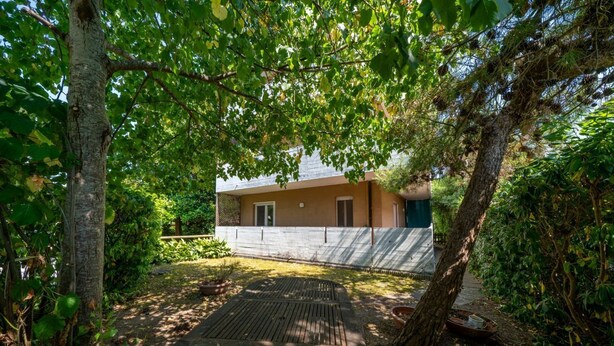 A house with a wooden deck, surrounded by trees and greenery. - GuestHost - Cozy 56 sqm ground-floor apartment featuring a balcony running along the entire perimeter and a private garden, perfect for relaxation and tranquility. Located in Grado Pineta, a green and quiet area just steps from the sea and nature trails, (Grado-Pineta)