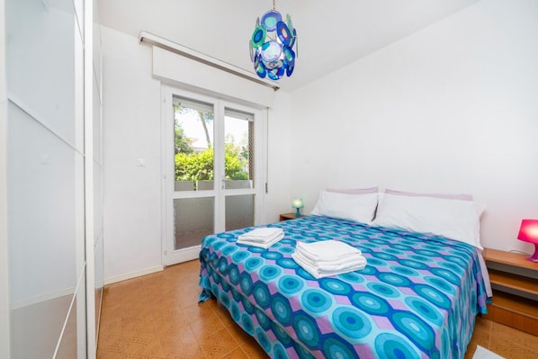 A bedroom with a bed, a door, a window, and a chandelier.