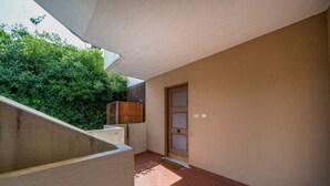 A narrow corridor with a wooden door, a concrete wall, and a brick floor. - GuestHost - Cozy 56 sqm ground-floor apartment featuring a balcony running along the entire perimeter and a private garden, perfect for relaxation and tranquility. Located in Grado Pineta, a green and quiet area just steps from the sea and nature trails, (Grado-Pineta)