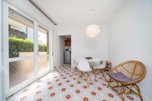 Un comedor con una mesa, sillas, una silla de mimbre, una lámpara colgante y vistas a través de un vidrio.