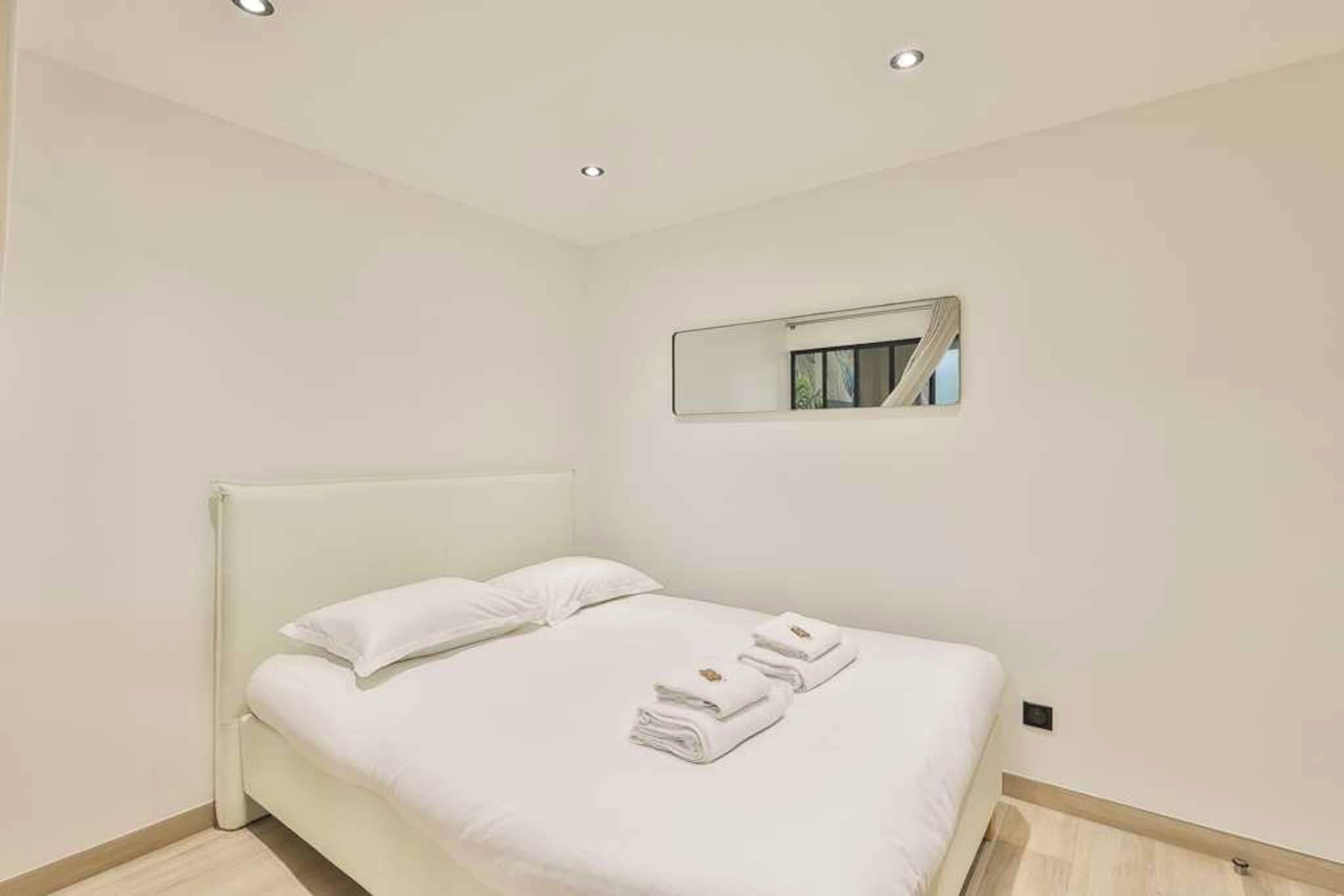 A modern bedroom with a single bed, a headboard, a wall-mounted mirror, and neatly folded towels on the bed.